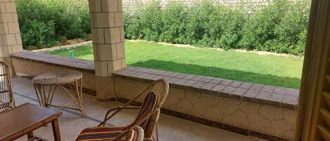 A covered patio area with a stone wall, a grassy lawn, and a view of the garden.