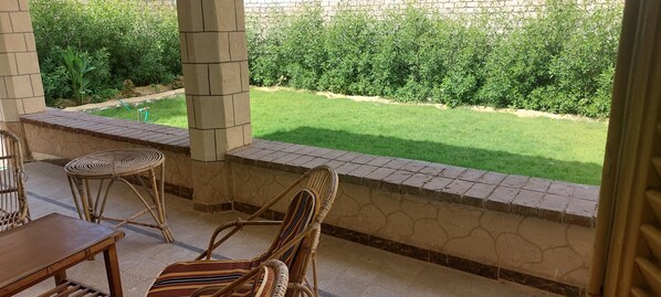 A covered patio area with a stone wall, a grassy lawn, and a view of the garden.