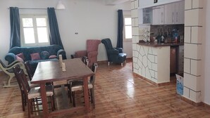A dining area with a wooden table and chairs, a sofa, and a kitchen area with cabinets and a countertop. - Holiday home for special people (El-Agamy)