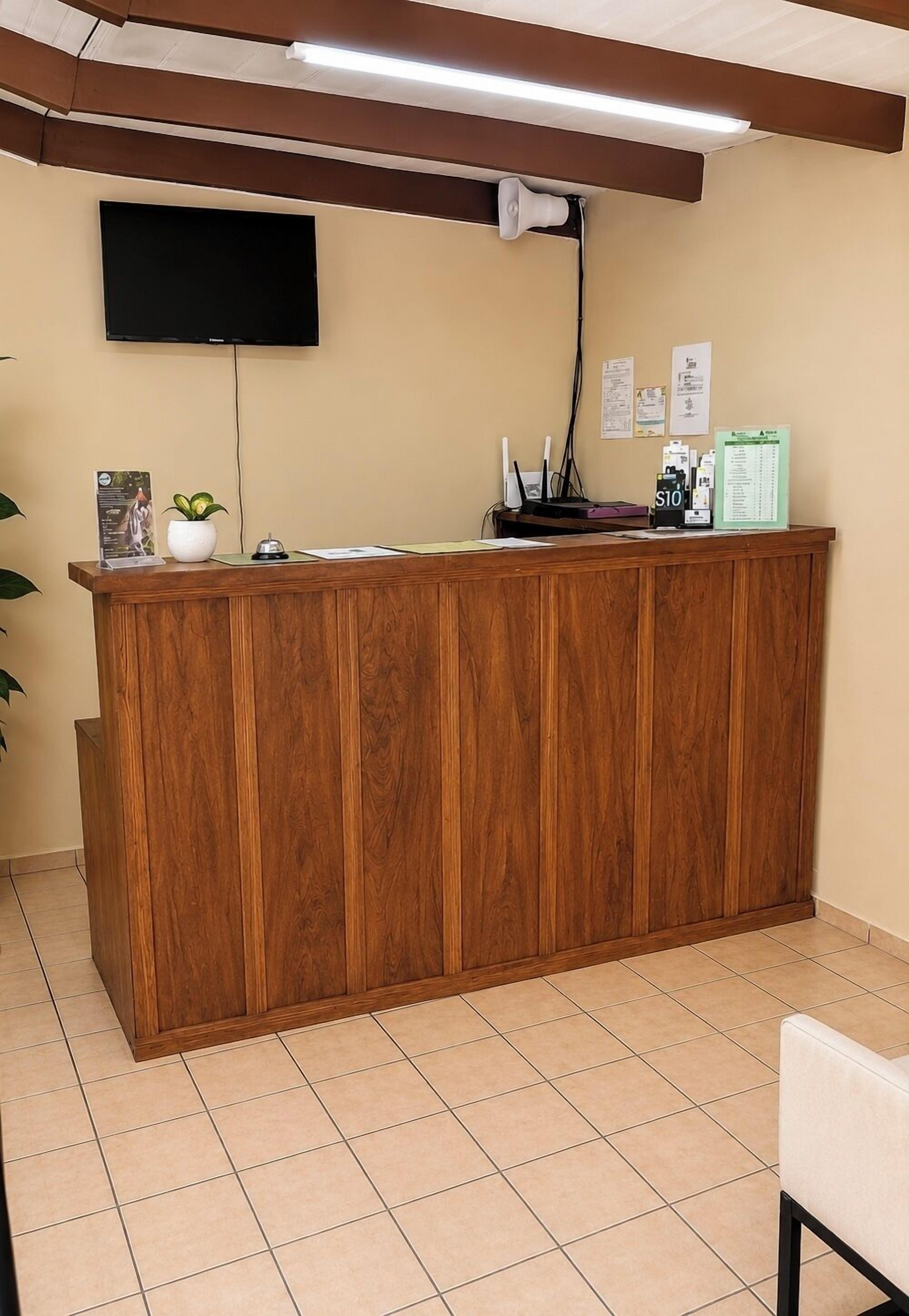 Een receptiebalie met een flatscreen televisie, een plant en informatiefolders aan de muur.