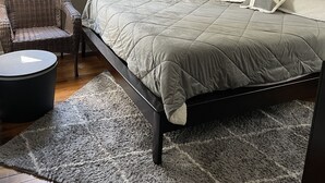 A bedroom with a bed, a chair, a rug, and a tiger painting on the wall.