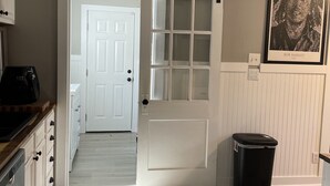 A hallway with a sliding door leading to a bedroom, a black trash bin, and a framed poster on the wall.