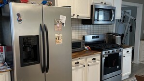 A kitchen with white cabinets, a stainless steel refrigerator, a microwave, an oven, and a coffee maker.