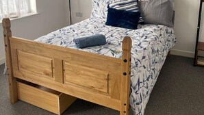 Una cama de madera con cabecera, una mesita de noche, un espejo y una ventana con cortinas.