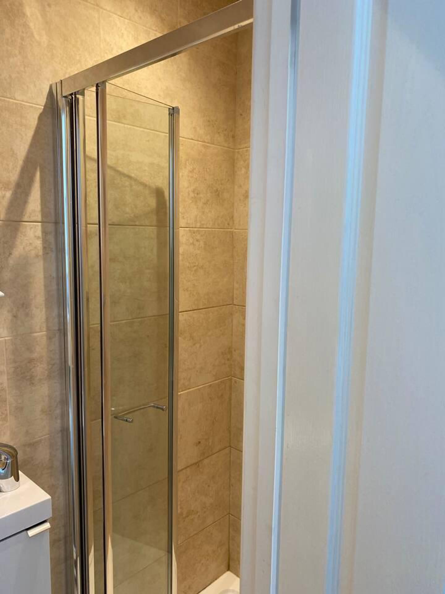 A glass-enclosed shower stall with a white sink and a towel rack to the left.