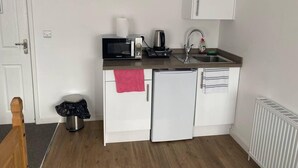 Una kitchenette compacta con microondas, cafetera, lavamanos y un refrigerador pequeño.