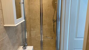 Ducha con cerramiento de vidrio, cabezal de ducha manual, lavabo blanco con grifo cromado y un mueble blanco sobre el lavabo.