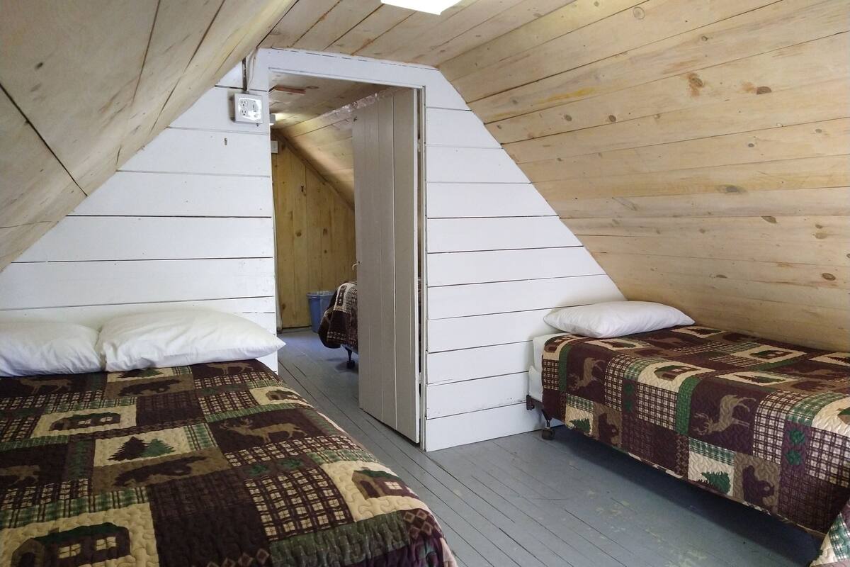 A room with two beds, a wooden ceiling, and a door leading to another room.