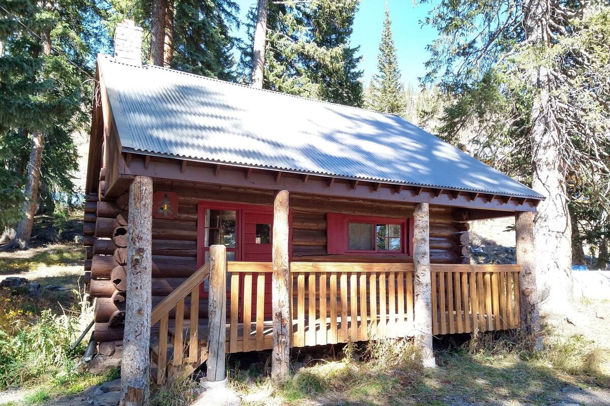 A rustic log cabin with a wooden porch and a red door.