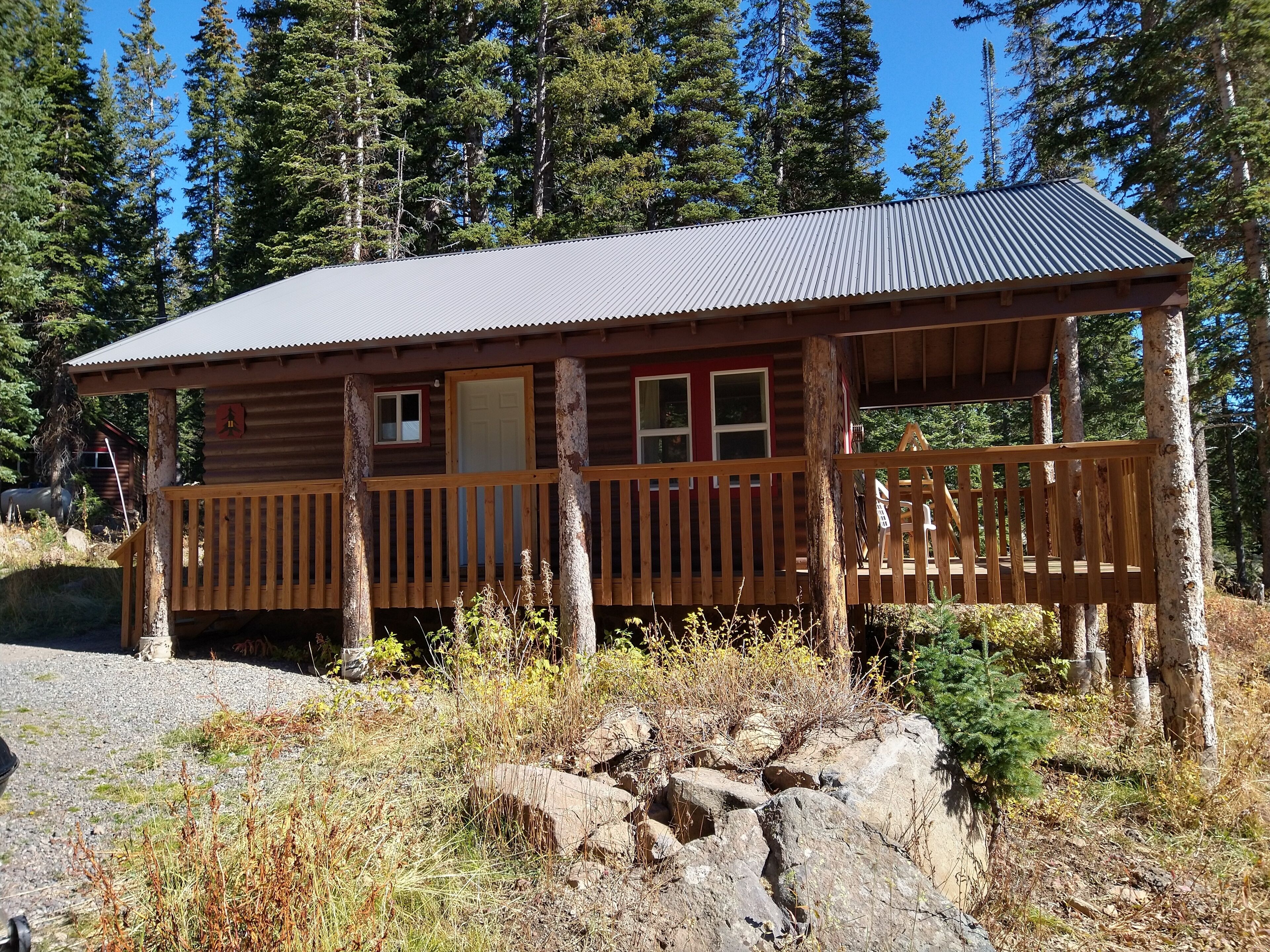 A rustic cabin with a wooden deck, a metal roof, and a door.