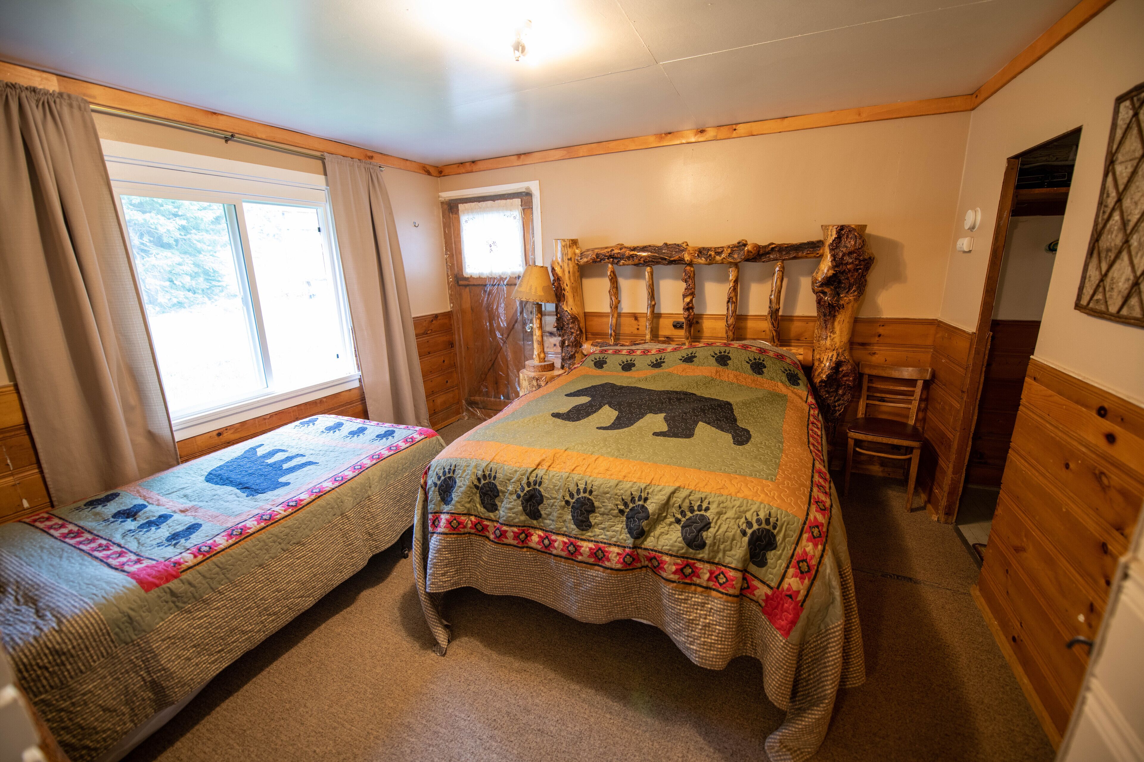 Un dormitorio con dos camas individuales, cabecero de madera, una ventana y una puerta.