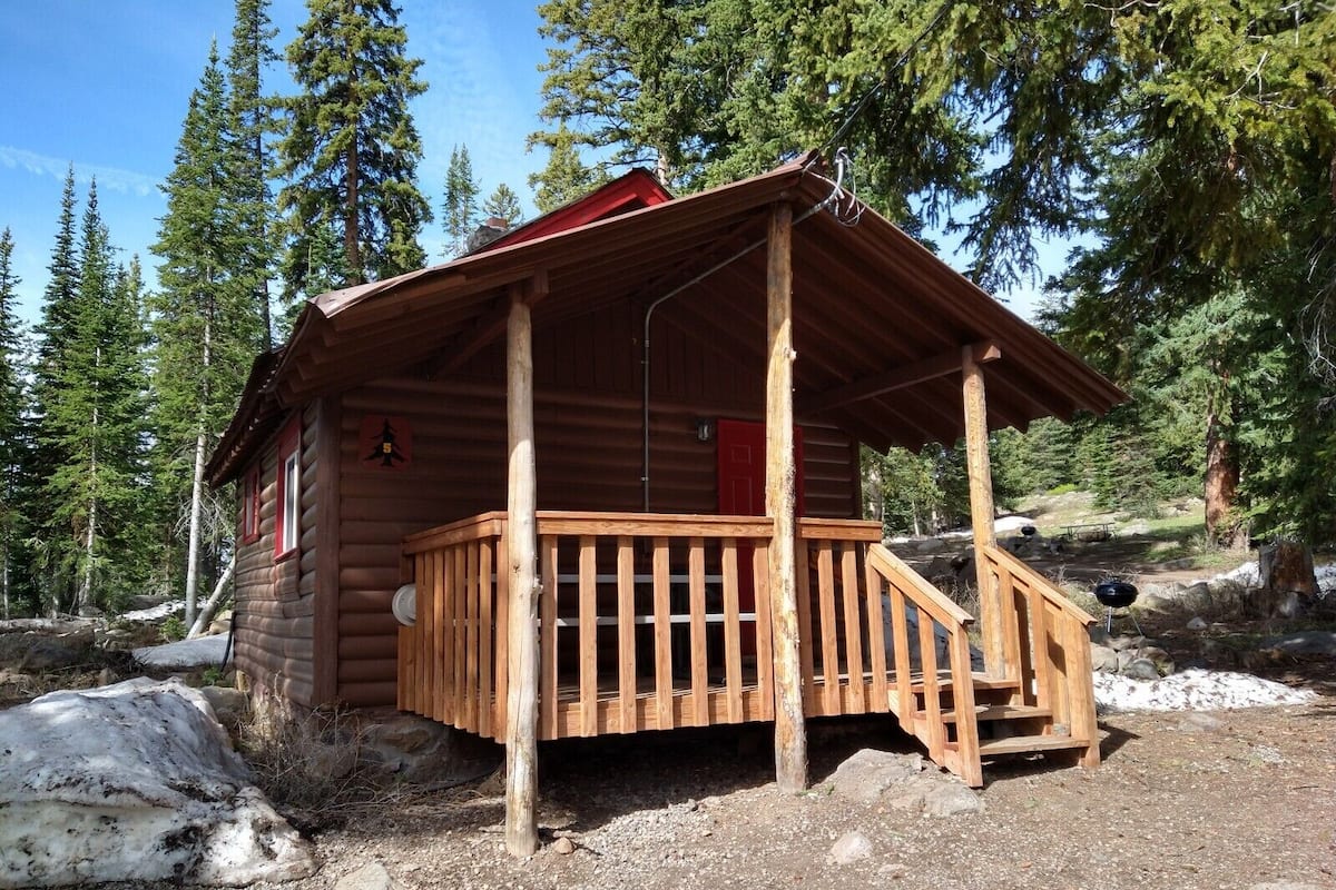A wooden cabin with a porch, surrounded by trees and rocky terrain.