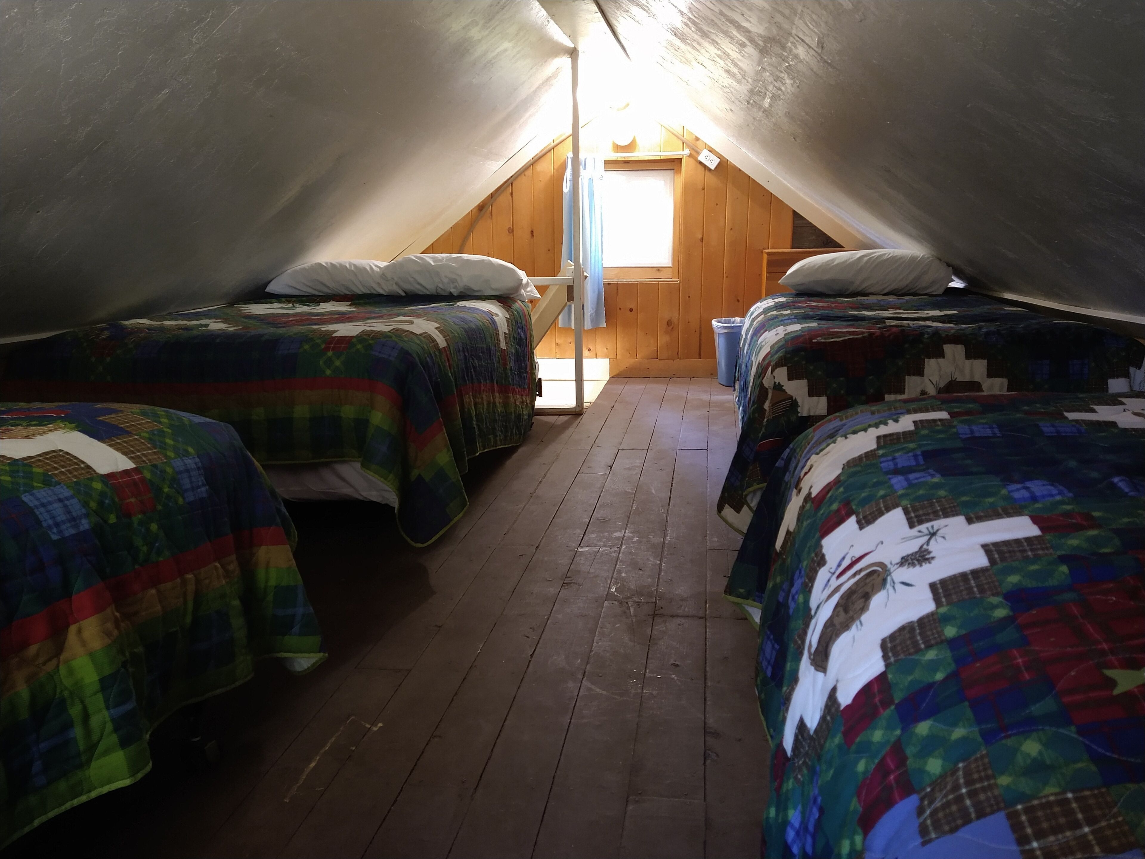 A small attic bedroom with three beds, wooden floors, and a sloped ceiling.