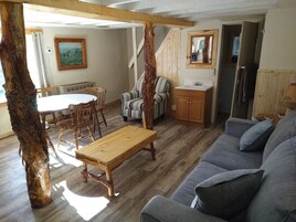 A rustic interior with a wooden dining table, a striped armchair, a gray sofa, and a wooden cabinet.