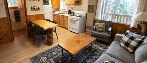 Un interior acogedor de cabaña con una mesa de comedor de madera, un sofá y una zona de cocina que incluye una estufa y armarios.