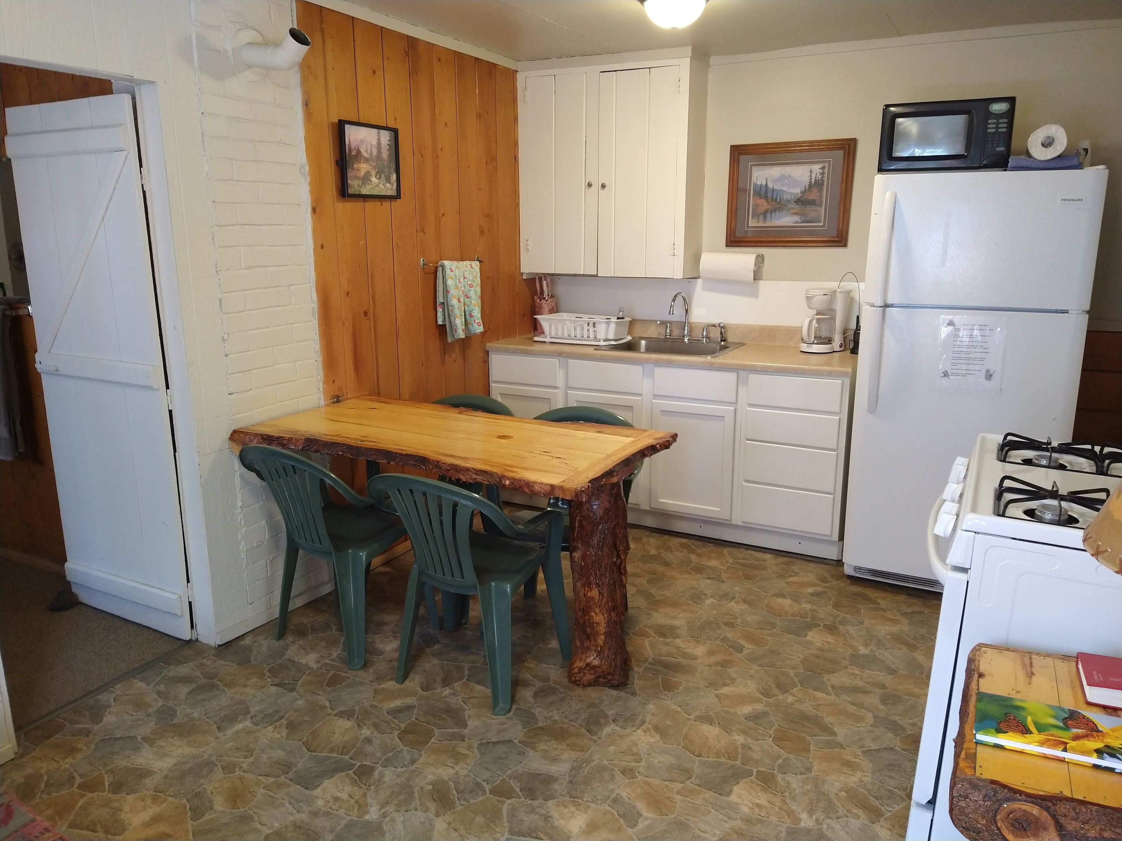 Una cocina compacta con una mesa de madera, sillas verdes, un refrigerador blanco, una estufa y un microondas.