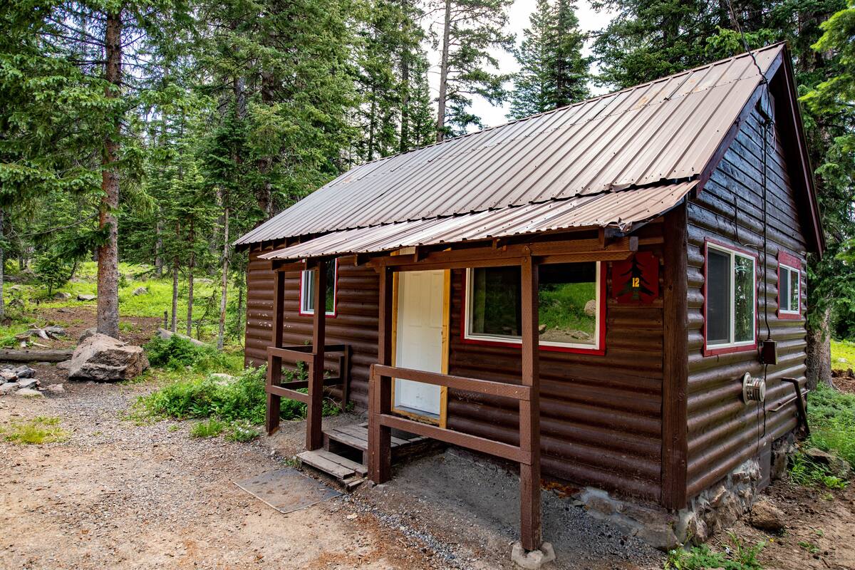 A rustic cabin with a wooden exterior, a metal roof, and a front porch.