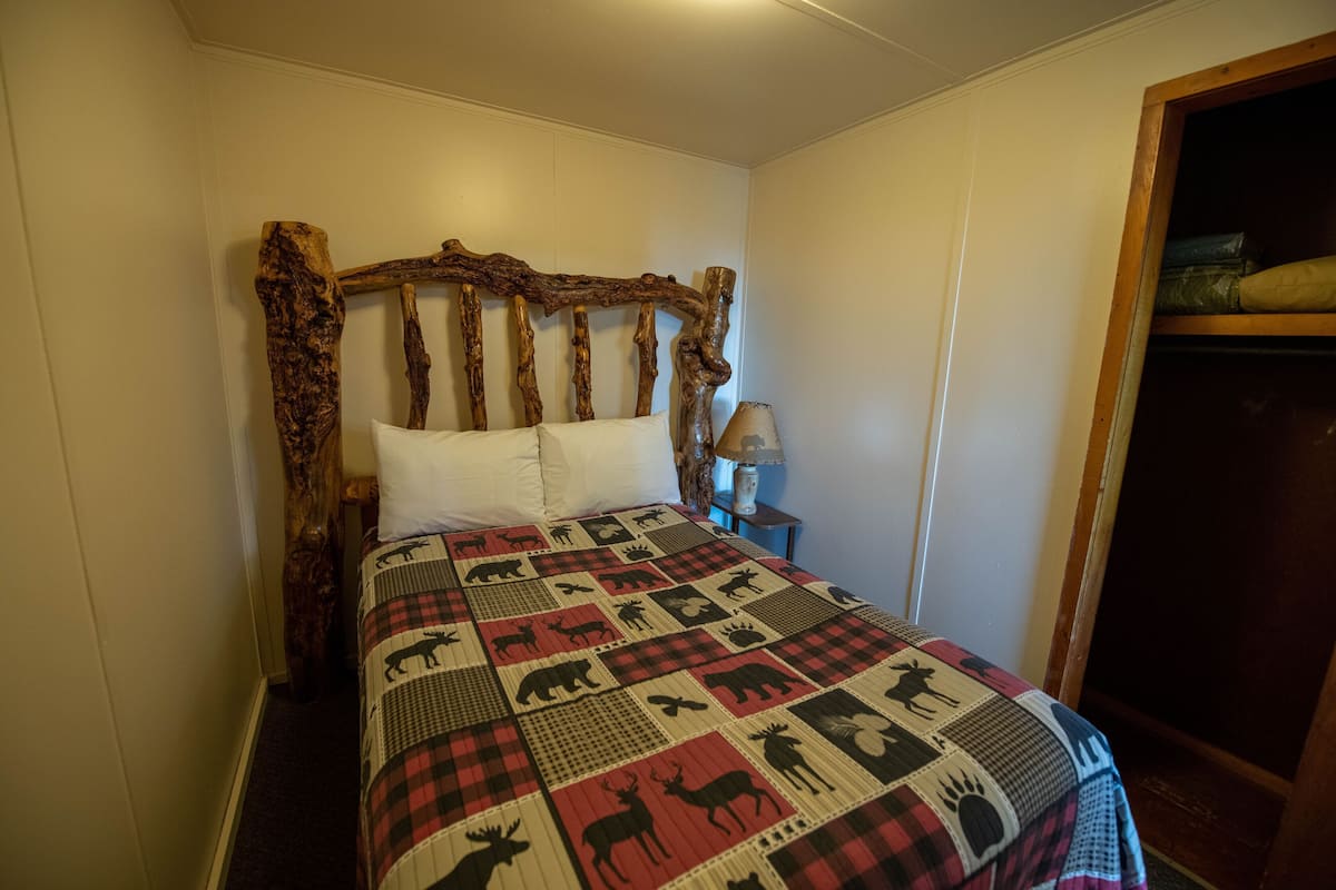 A bed with a wooden headboard, a quilt with animal prints, and a nightstand with a lamp.