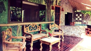 A wooden bench and table set against a wall with a tropical mural, a stone wall with a window, and a thatched roof. - Contemporary Villa in a Four‑Acre Tropical Urban Park, Osa Peninsula (Puerto Jiménez)