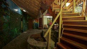 A staircase with wooden steps and a bamboo handrail, leading to a room with a mural and a door. - Contemporary Villa in a Four‑Acre Tropical Urban Park, Osa Peninsula (Puerto Jiménez)