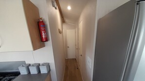 Ett smalt kök med ett kylskåp i rostfritt stål, en gasspis och en brandsläckare som är monterad på väggen.