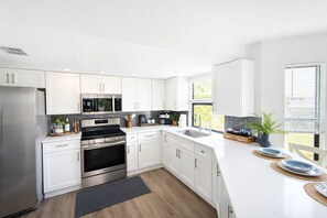 A modern kitchen with white cabinets, stainless steel appliances, and a large window providing natural light.