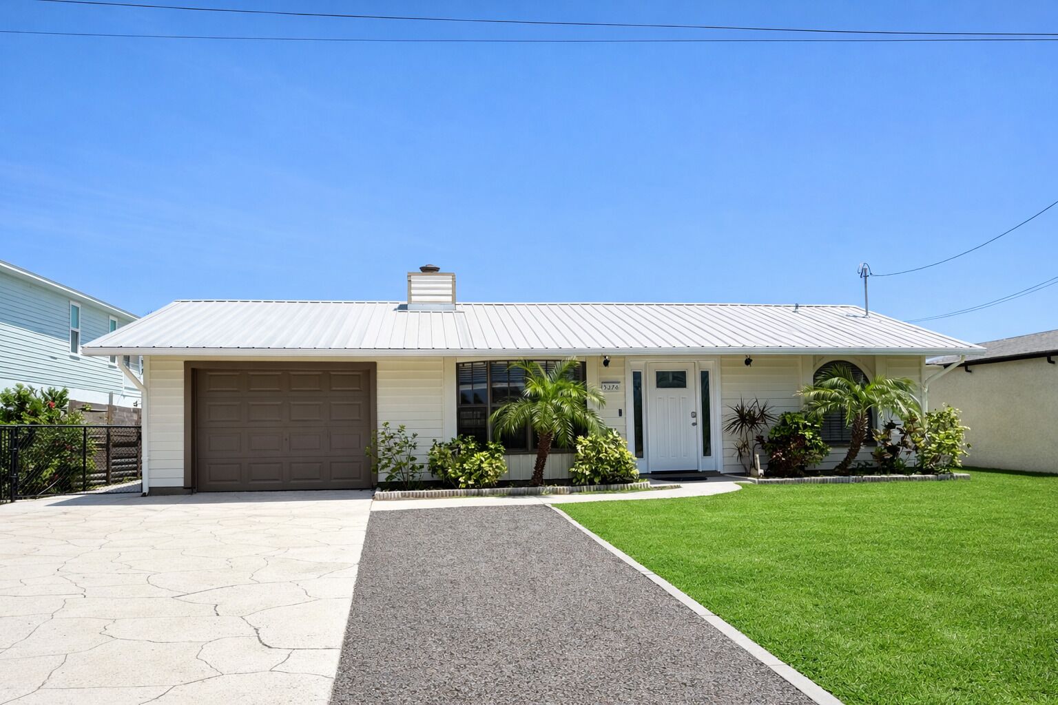 A single-story building with a garage, a front door, and a small porch with plants.