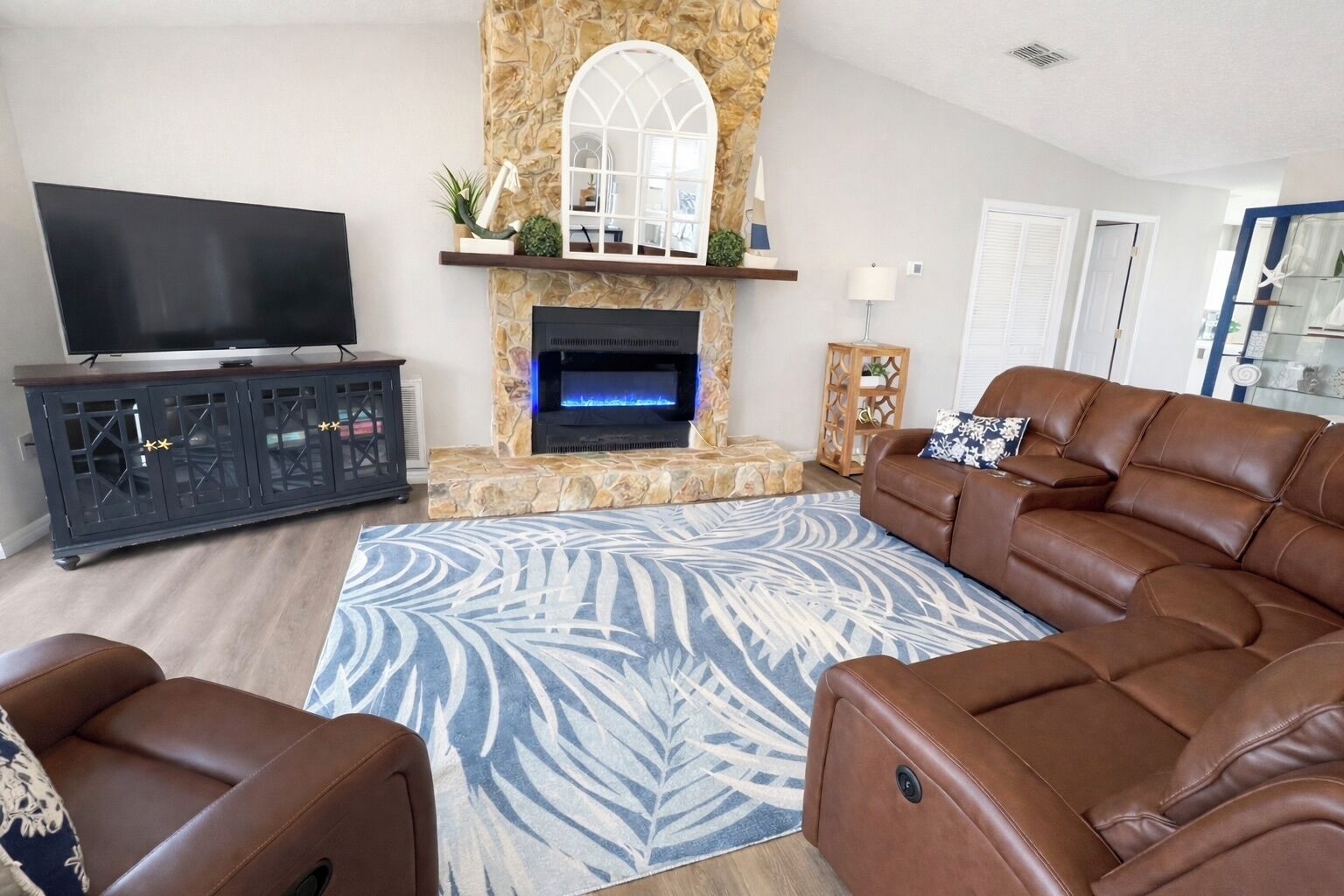 A living room with a stone fireplace, leather sofa, and a flat-screen TV.
