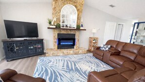 A living room with a stone fireplace, leather sofa, and a flat-screen TV. - Paradise - Golf Cart Rental, Kayaks, Paddle Boat, Fishing & Swimming (Hernando Beach)