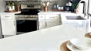 A modern kitchen with white cabinets, stainless steel appliances, and a central island with white plates and woven placemats. - Paradise - Golf Cart Rental, Kayaks, Paddle Boat, Fishing & Swimming (Hernando Beach)