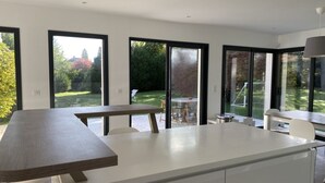 Een moderne keuken met een centraal kookeiland, grote ramen en uitzicht op een tuin.