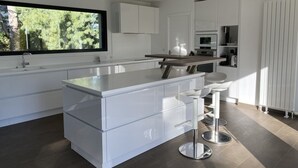 Een moderne keuken met witte kasten, een groot eiland met barstoelen en een raam met uitzicht op groen.