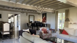 Een ruime woonkamer met een hoge plafond, een kroonluchter, een piano en een bank.