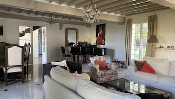 A spacious living room with a high ceiling, a chandelier, a piano, and a sofa.