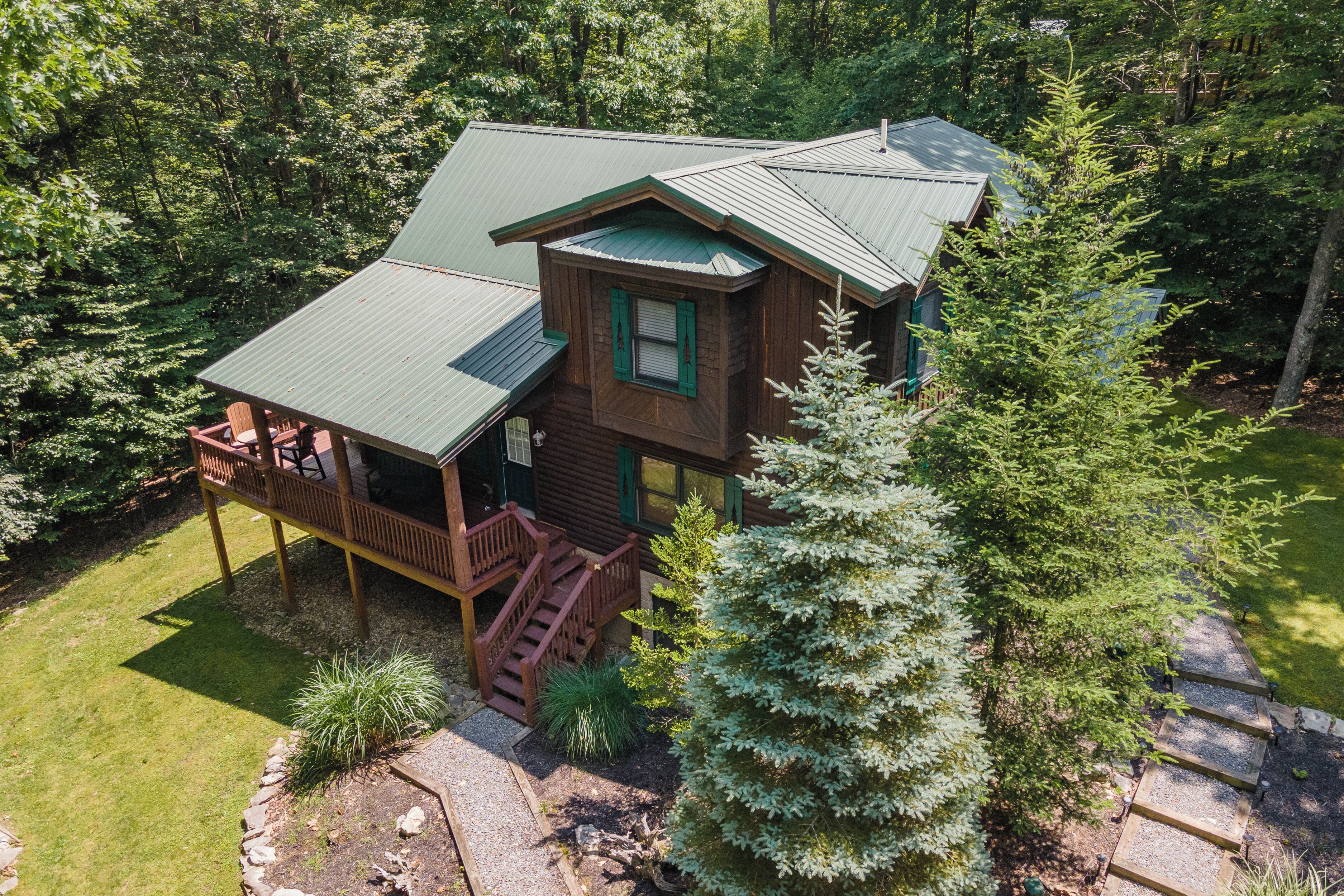 A cabin with a deck and stairs, surrounded by trees and a well-maintained lawn.