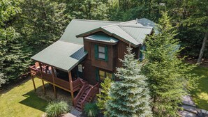 Une cabane dotée d’une terrasse et d’un escalier, entourée d’arbres et bordée d’une pelouse bien entretenue.