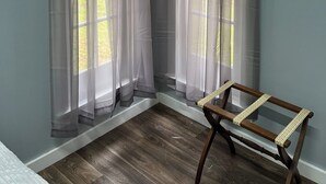 A room with two windows featuring sheer curtains, a wooden bench, and a view of greenery outside.