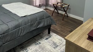 A bedroom with a bed, a chair, a wooden desk, and sheer curtains.
