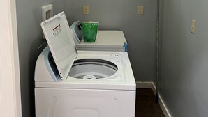 A laundry room with a front-loading washer and dryer, a green laundry basket, and a framed sign on the wall.