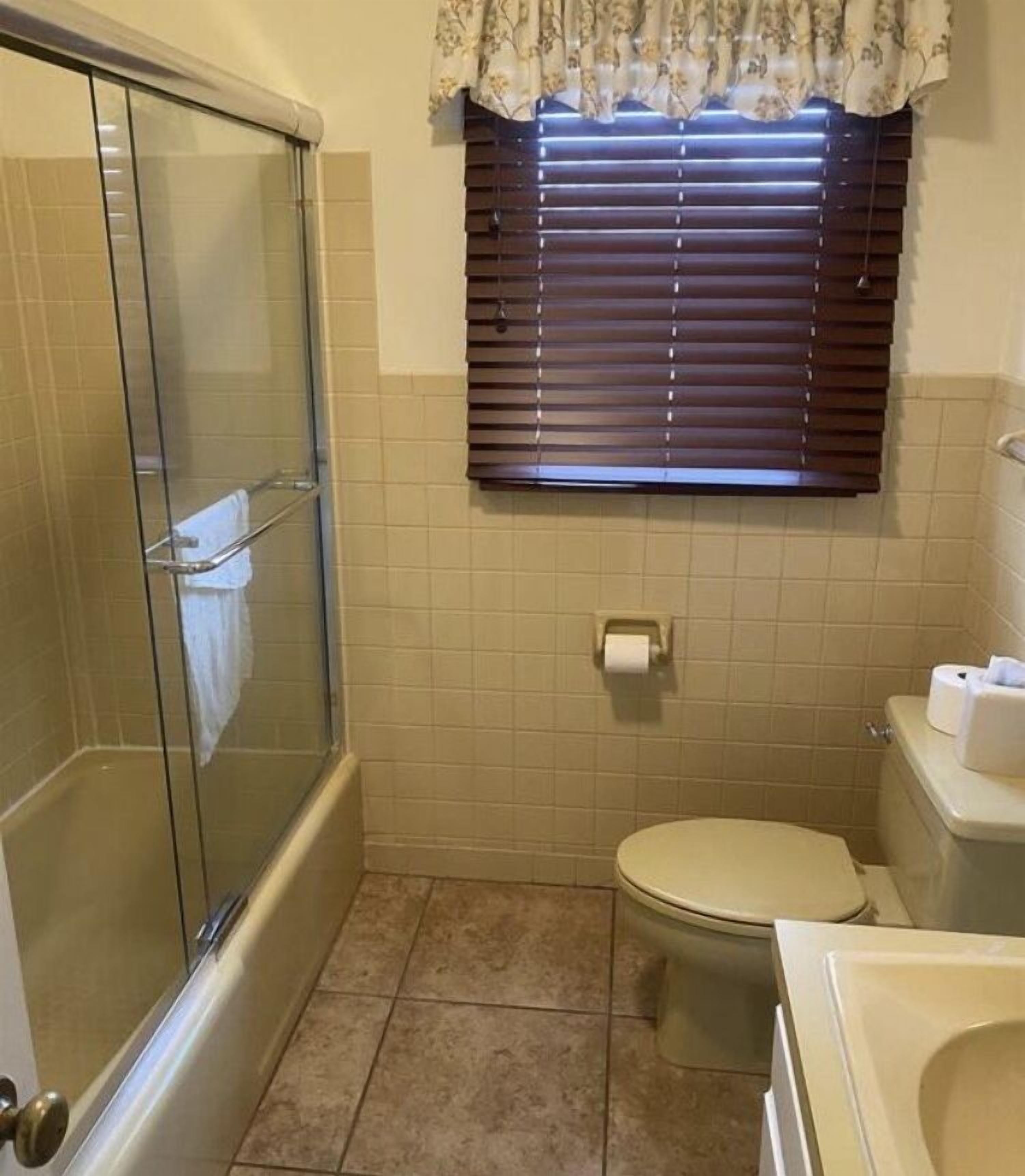 A bathroom with a glass-enclosed shower, a toilet, and a window with blinds.