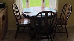 A dining area with a round table and four chairs, a window with curtains, a ceiling fan, and a wall-mounted picture.
