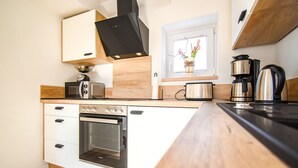 Una cucina compatta con mobili bianchi, forno integrato, microonde, macchina del caffè e tostapane.