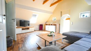 Un accogliente spazio abitativo mansardato con pavimento in legno, una TV, un'area pranzo e un divano grigio.