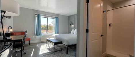 Een moderne slaapkamer met een bed, nachtkastje en bureau met stoel. Er is een raam met gordijnen, een radiator en een deur naar een andere kamer.