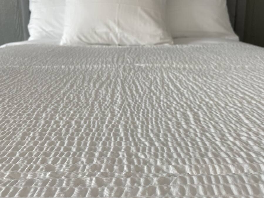 Een bed met een ribbeltextuur wit dekbed en twee kussens, geplaatst tegen een houten hoofdbord.