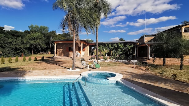 Una piscina con solarium in pietra, un'area salotto coperta e una casa con facciata in pietra.