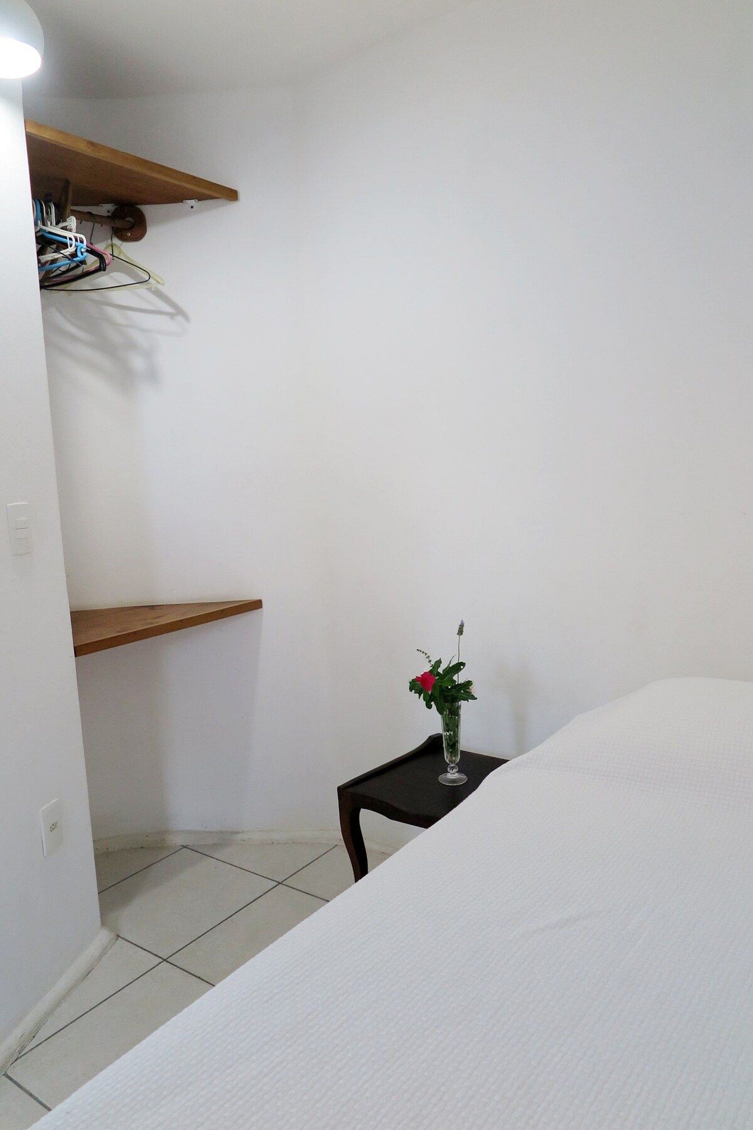 Un dormitorio con una cama, una mesita de noche con un florero y una estantería de madera.