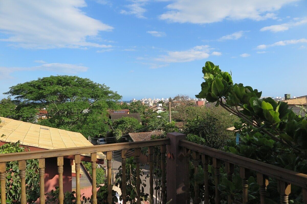 A view from a balcony with a wooden railing, overlooking a residential area with houses and trees under a clear sky.