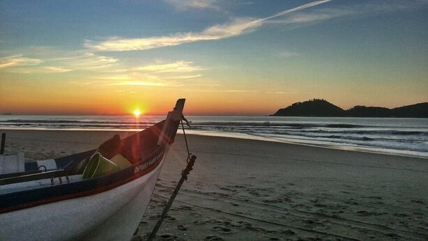 A boat on a beach with a sunset in the background. - Pousart Floripa (Florianópolis)