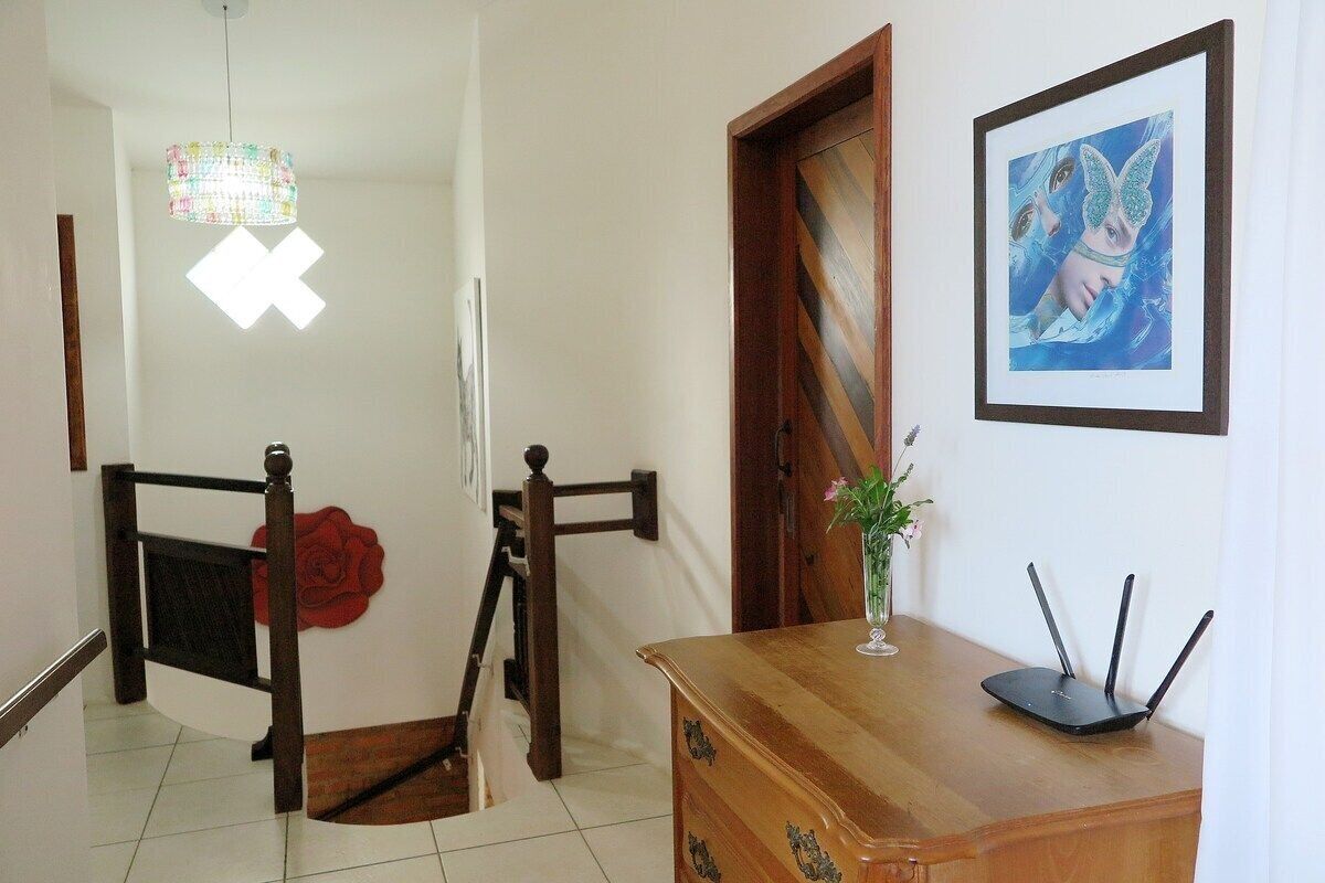 Un pasillo con una escalera, un armario de madera, una obra de arte enmarcada y un accesorio de iluminación decorativo.